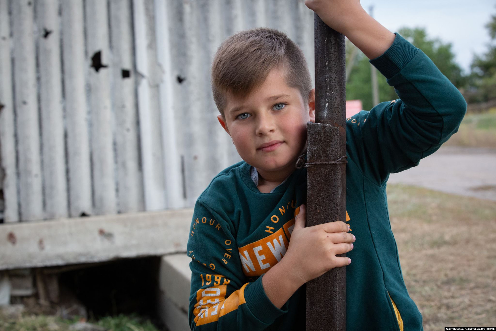 Davyd, 10, wants to be a lawyer and to go to sea. The fence behind their house in Luhanske is full of holes from a mine explosion. (photo: Andriy Dubchak)