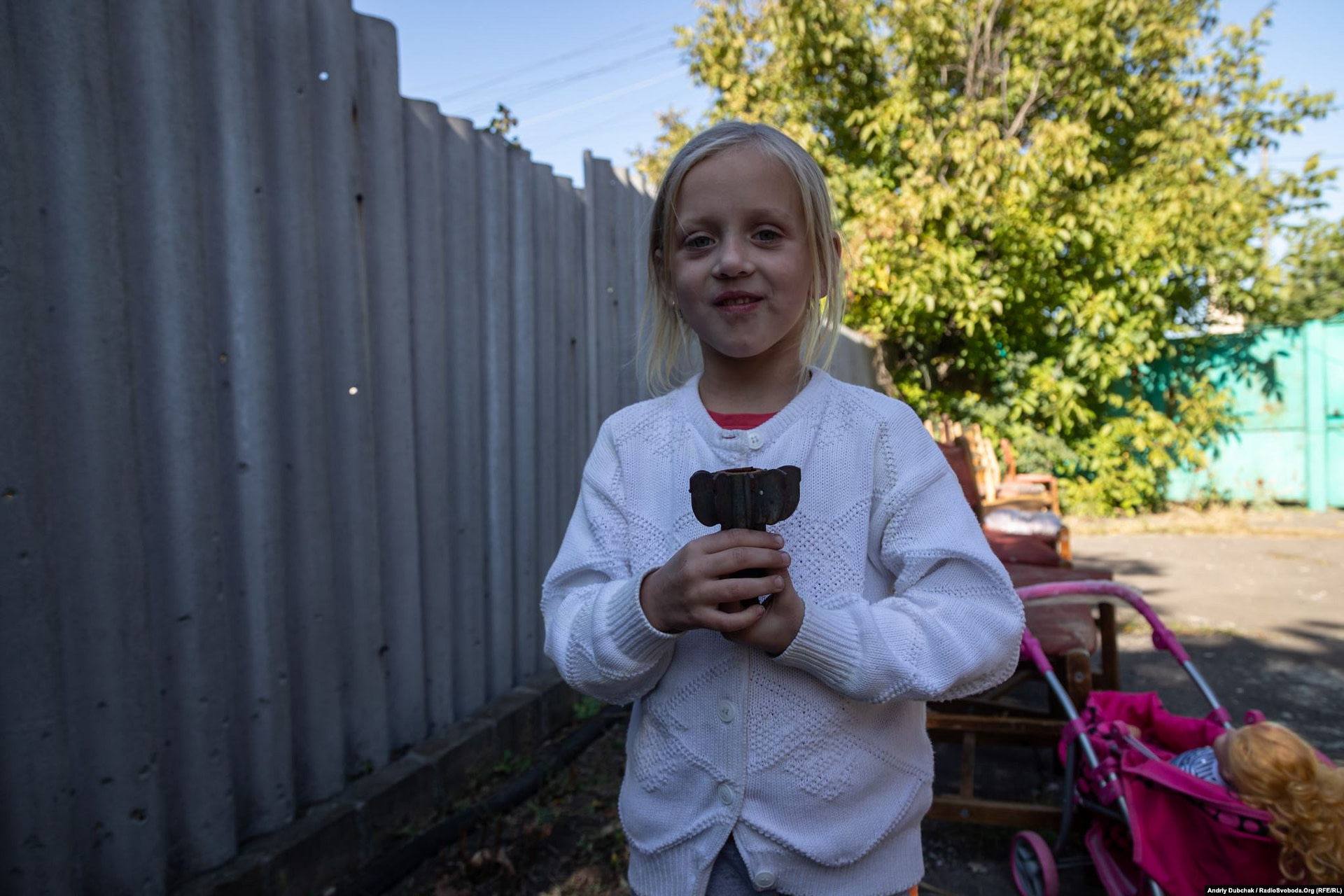 Toma holds part of the shell in a neighbor's yard, where her sister and brother were injured in Maryinka. (photo: Andriy Dubchak)