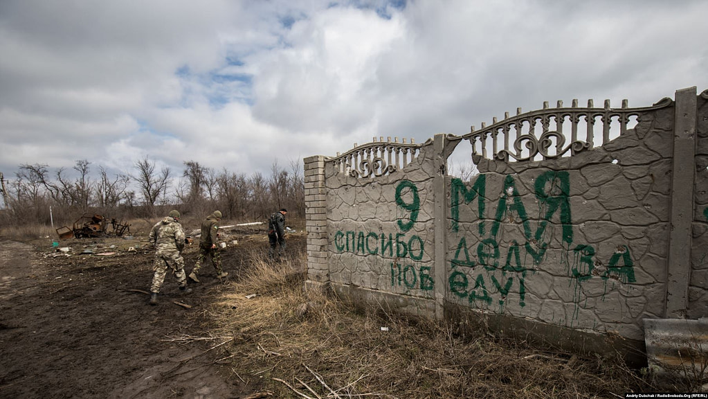 Ukrainian soldiers walk past a fence in Shyrokyne with a message written by Russia-backed separatists: “May 9, Thank your grandfather for the victory!” in reference to the 1945 Soviet victory over Nazi Germany. Photo Andriy Dubchak